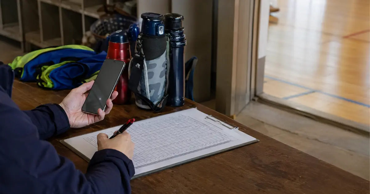 体育館脇で、スマートフォンと出欠表を照合するスタッフの手元。